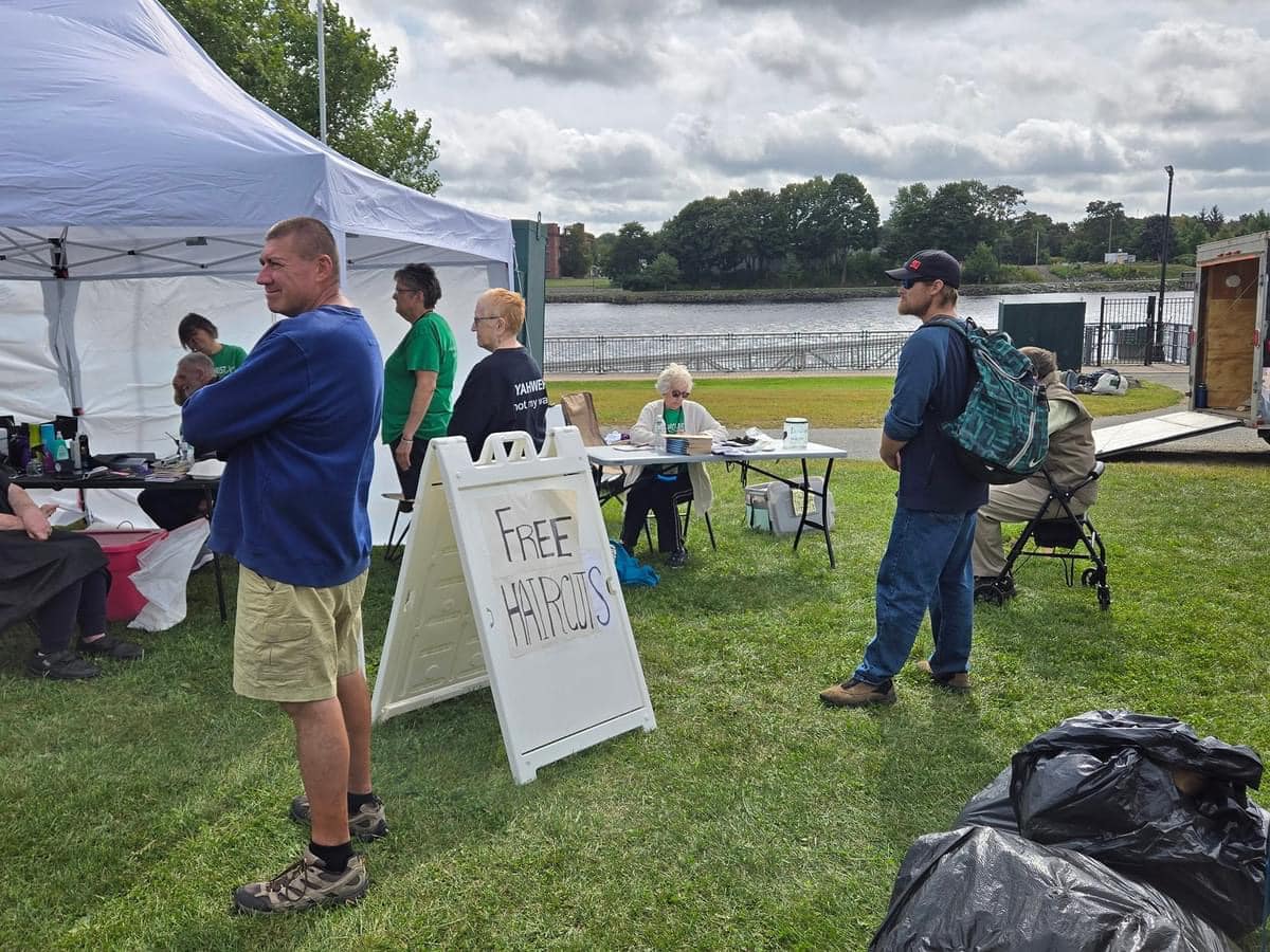 A group of people gathered around a sign: free haircuts